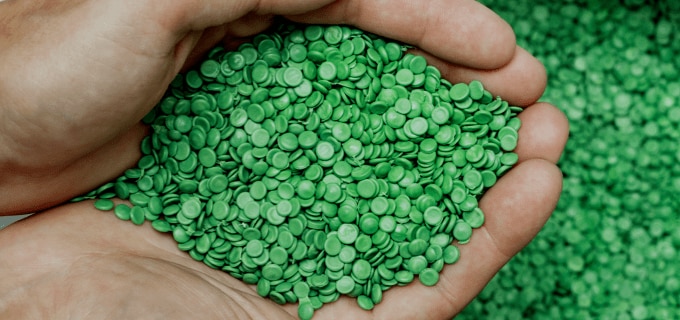 Hände mit grünem Plastikgranulat auf den Handflächen